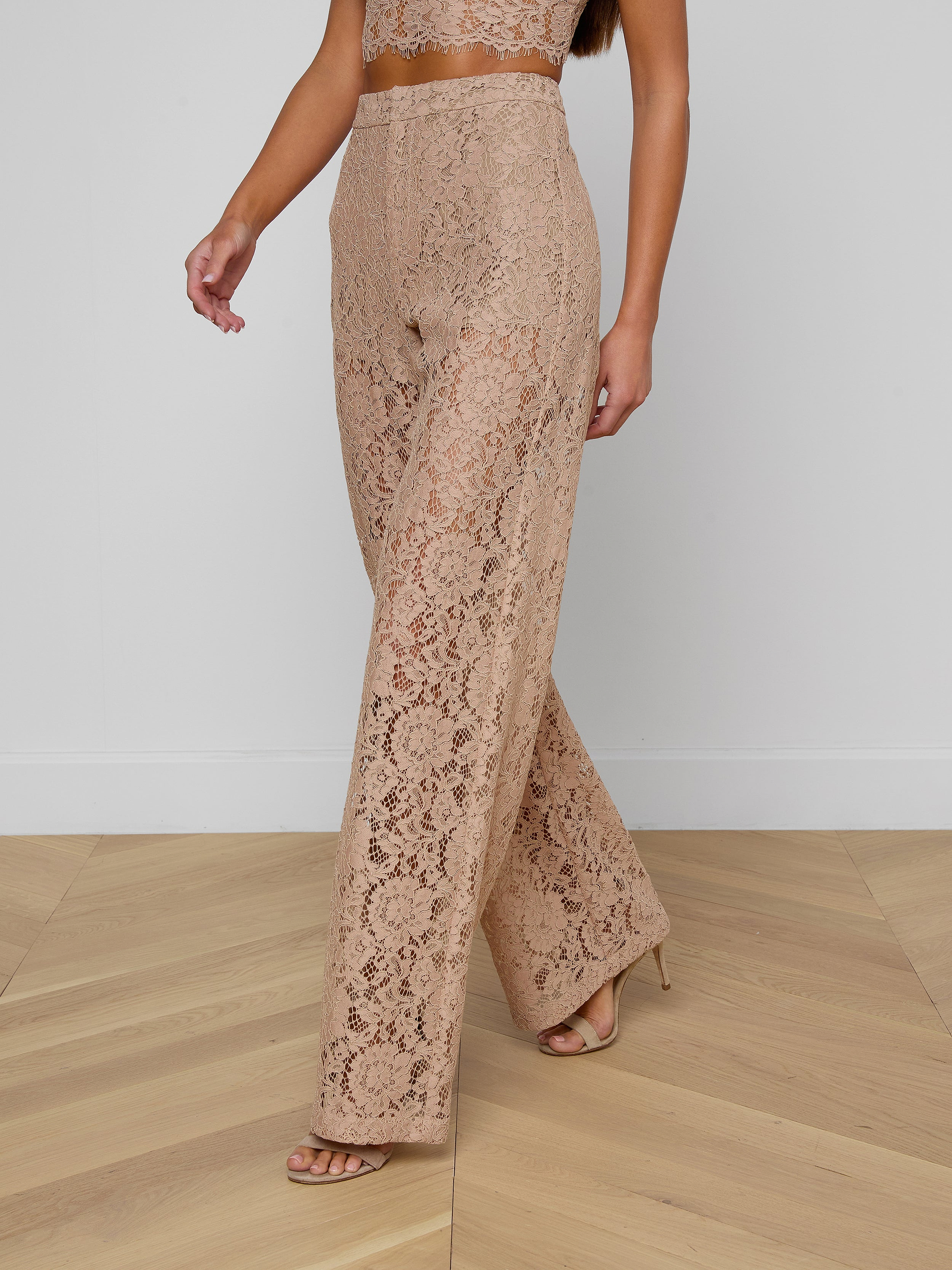 A woman is wearing the Livvy Lace Trouser—beige, high-rise, straight-leg pants with a floral lace pattern—paired with a matching crop top and nude heels. Only her body from the shoulders down is visible against a plain background.