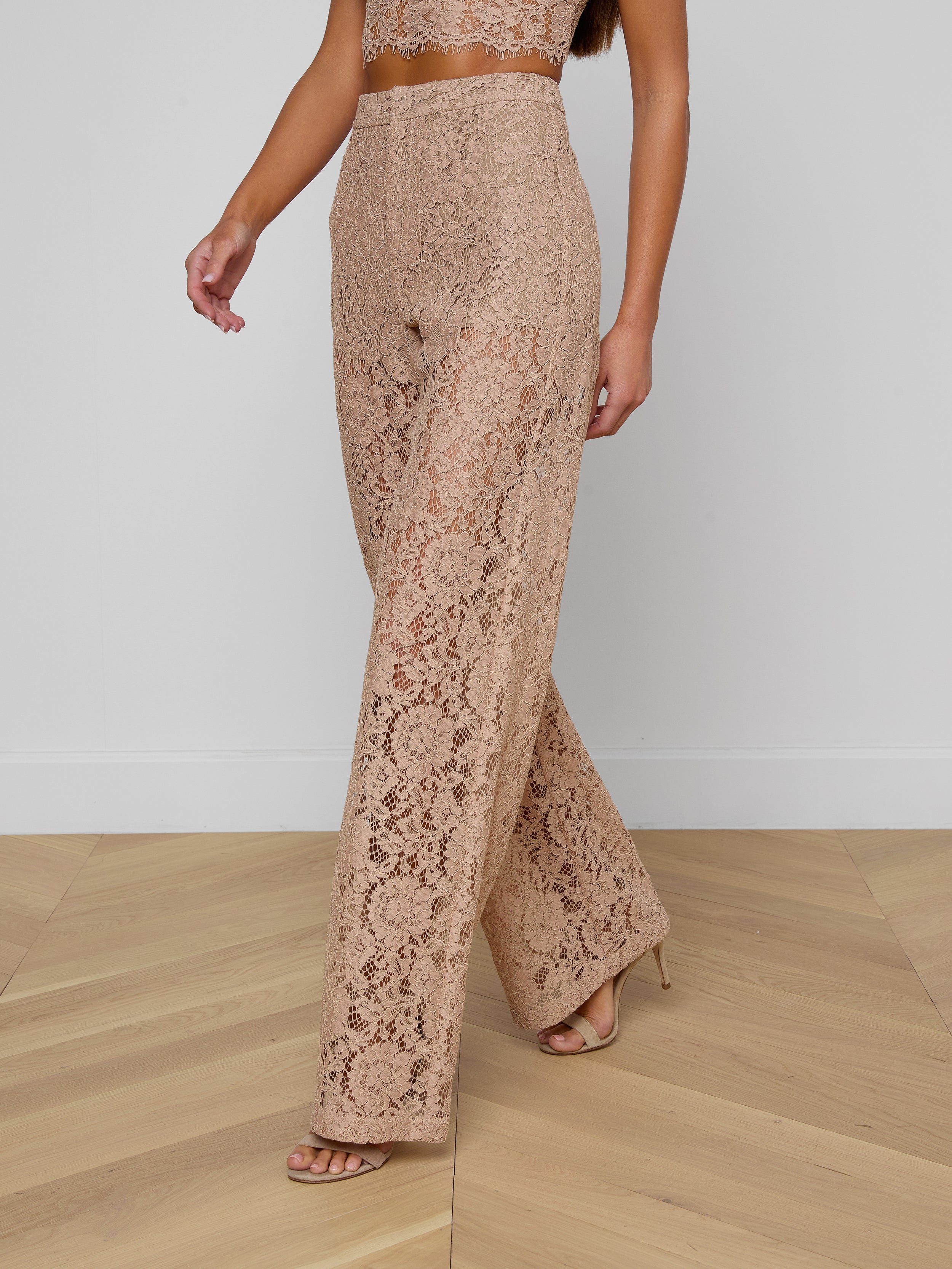 A woman is wearing the Livvy Lace Trouser—beige, high-rise, straight-leg pants with a floral lace pattern—paired with a matching crop top and nude heels. Only her body from the shoulders down is visible against a plain background.