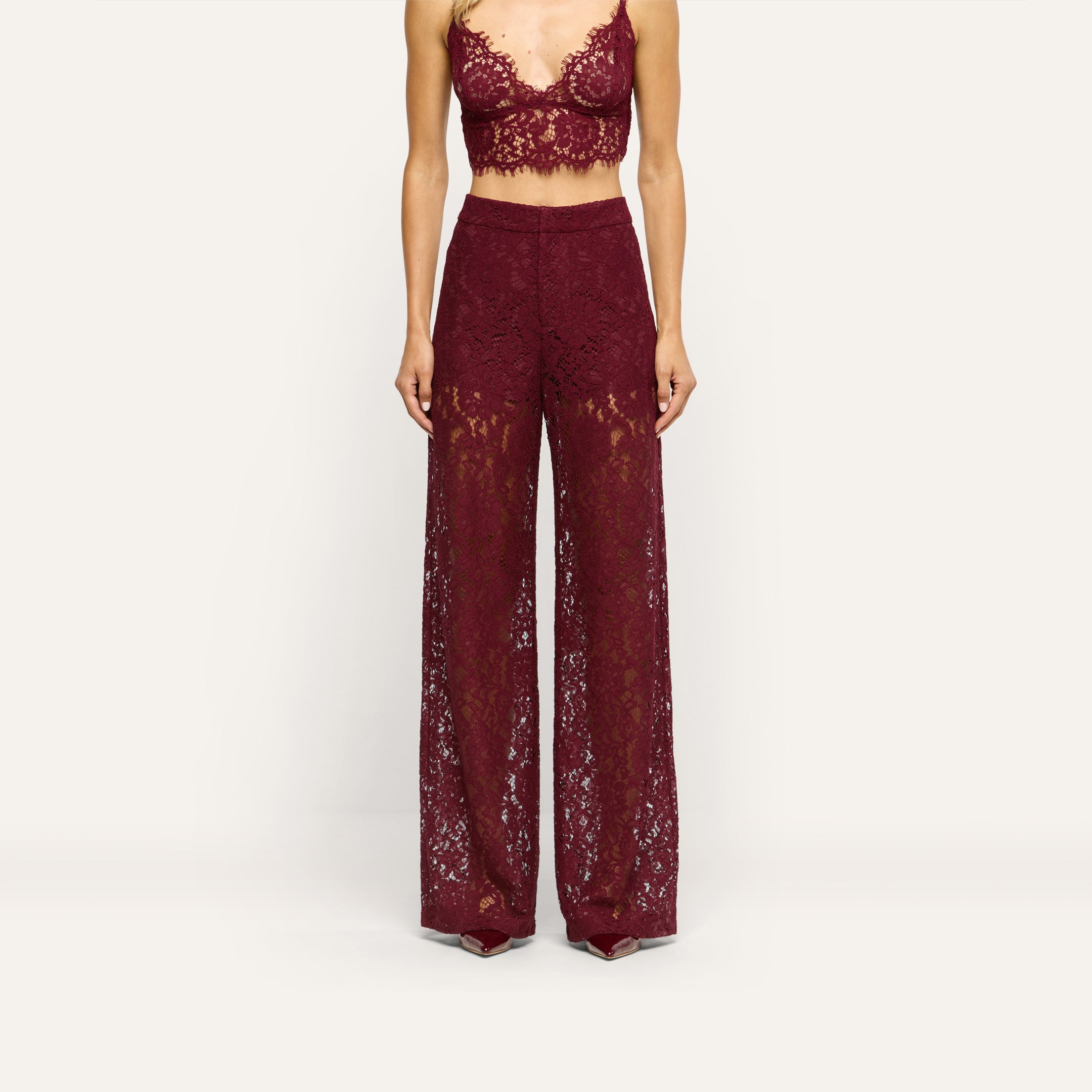 A person wears deep burgundy Livvy Straight-Leg Trousers in floral lace, paired with a matching lace crop top.