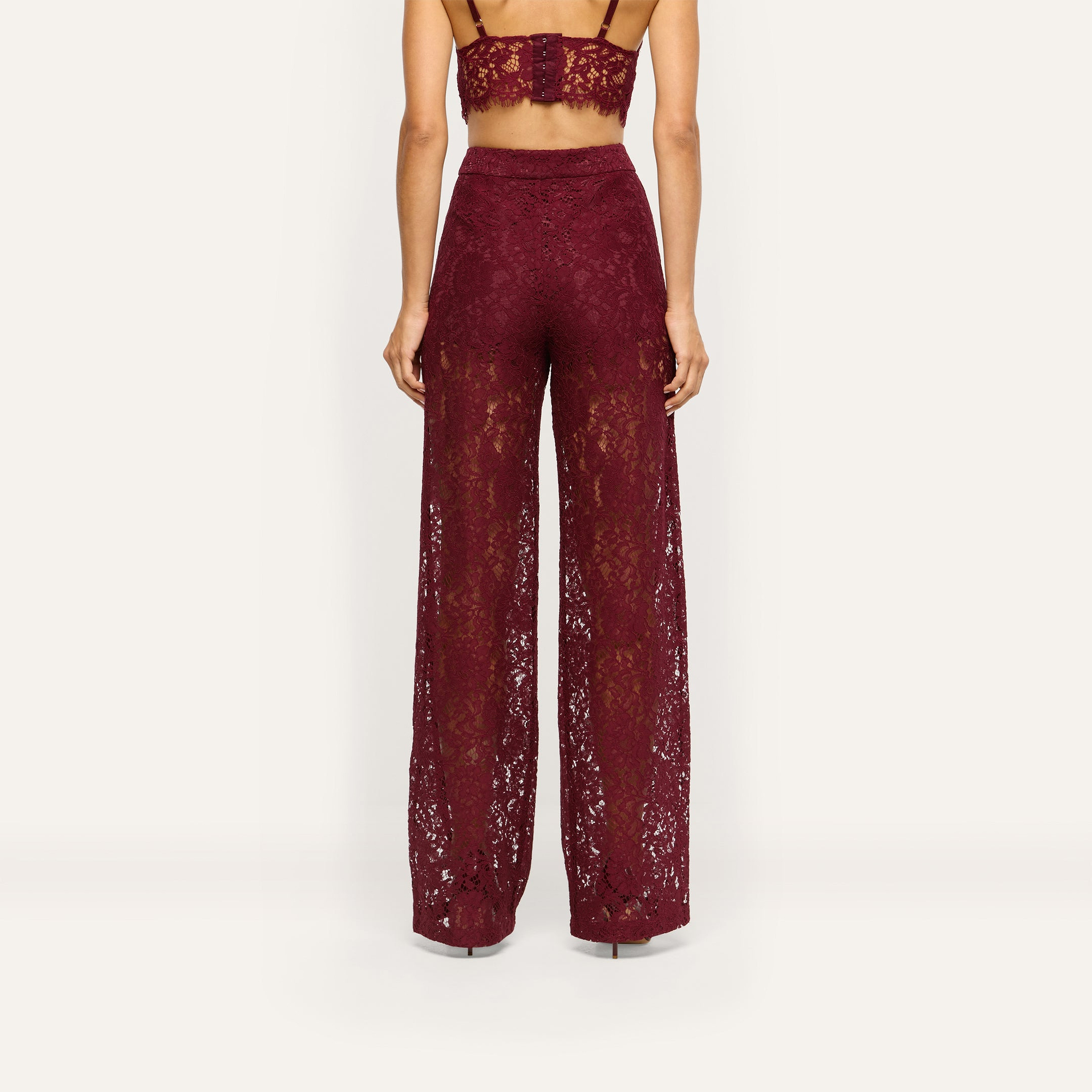A person from the back wearing burgundy floral lace Livvy Straight-Leg Trousers and a matching lace bralette.