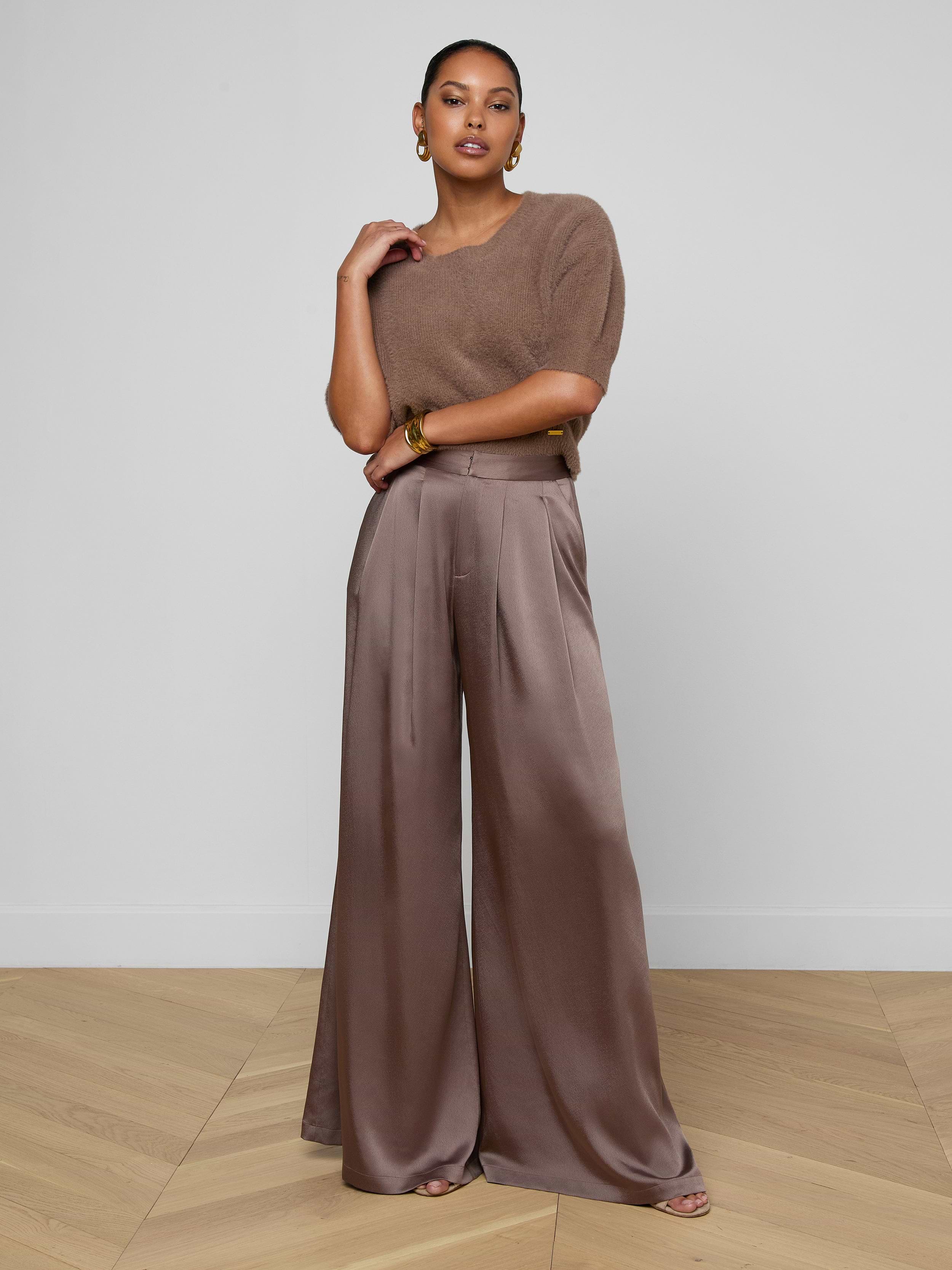A woman stands against an off-white background, wearing a cardamom brown short-sleeve knit top paired with the Aubrie Satin Pant—a high-waisted, wide-leg trouser in a matching shade—styled with large earrings and open-toe shoes.