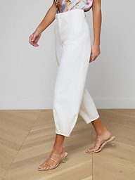 A woman wearing the Krista Tapered Jean in white, a floral sleeveless top, and beige heeled sandals stands against a plain light background. Her face is not visible.