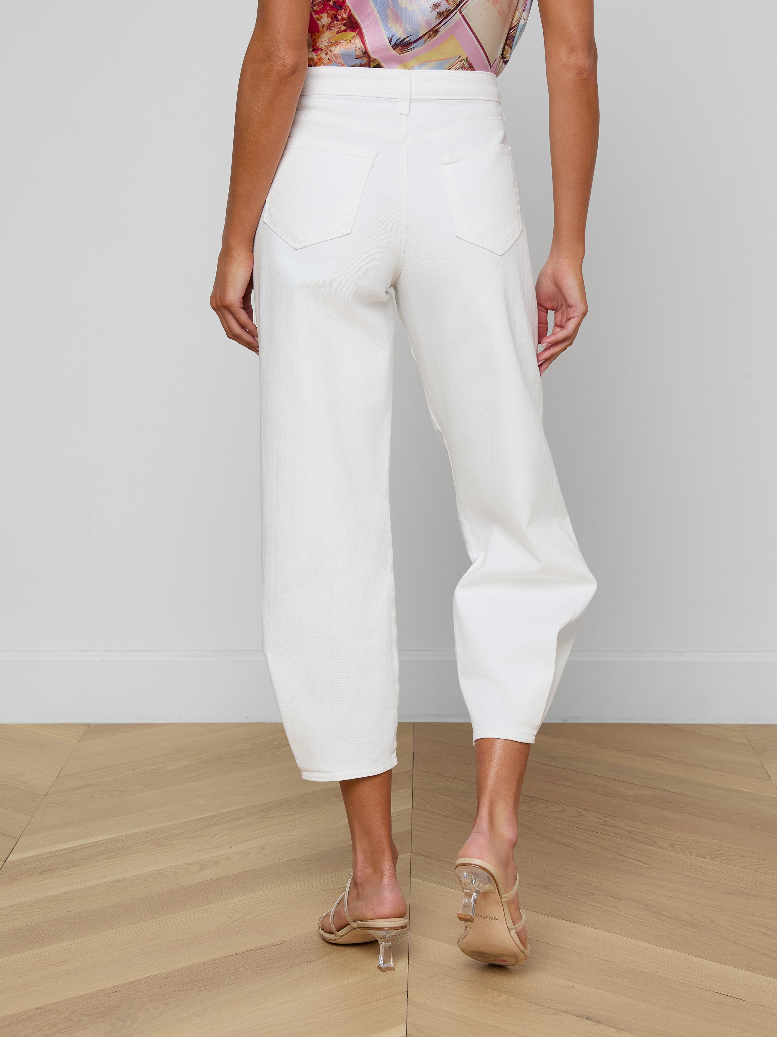 Wearing the Krista Tapered Jean, which features a white high-rise tapered leg in stretch denim, and heeled sandals, a person stands with their back to the camera against a plain light background.