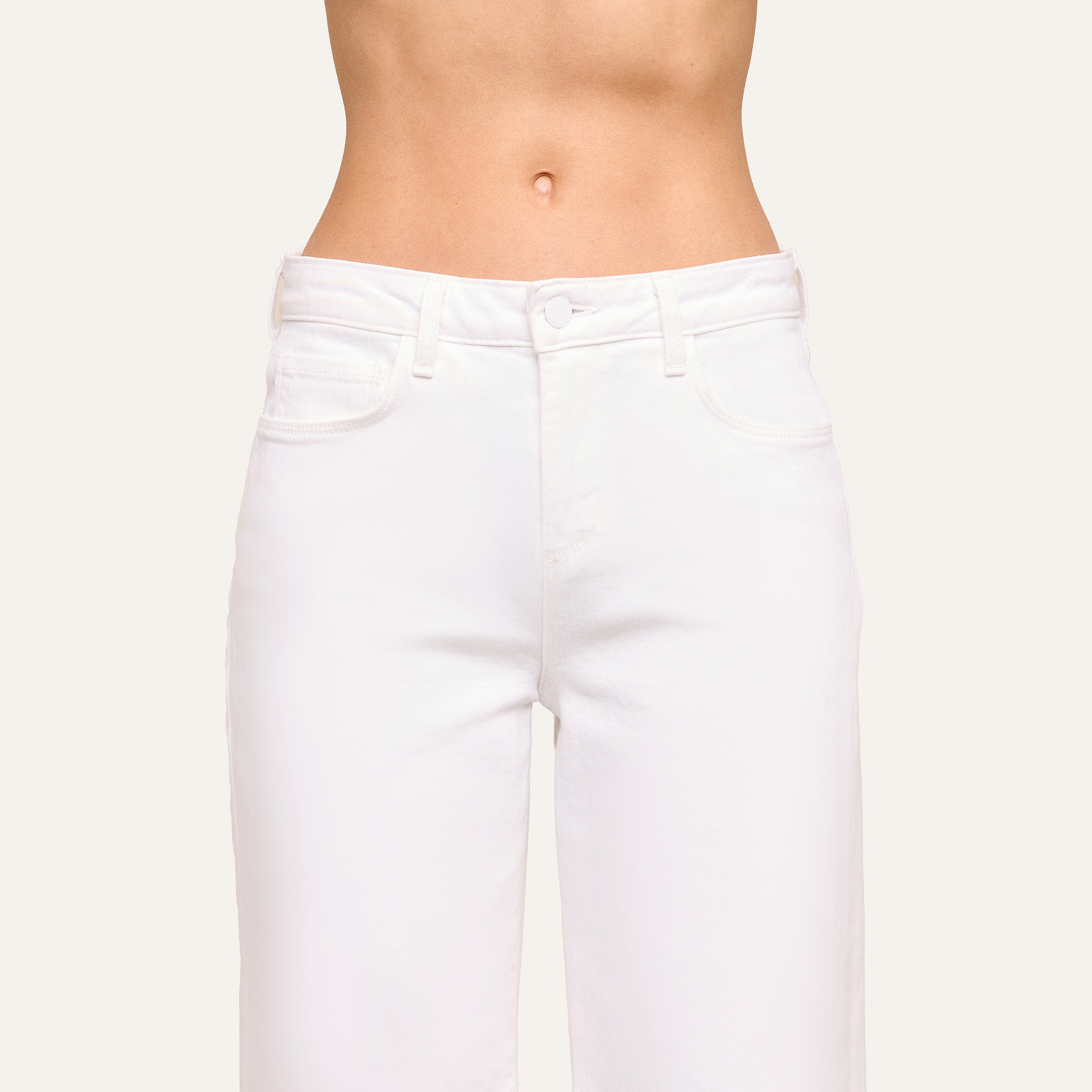 A close-up of a person wearing the Krista Tapered Jean in white, highlighting the high-rise waist and upper legs with a visible bare midriff; face and upper body are not shown.