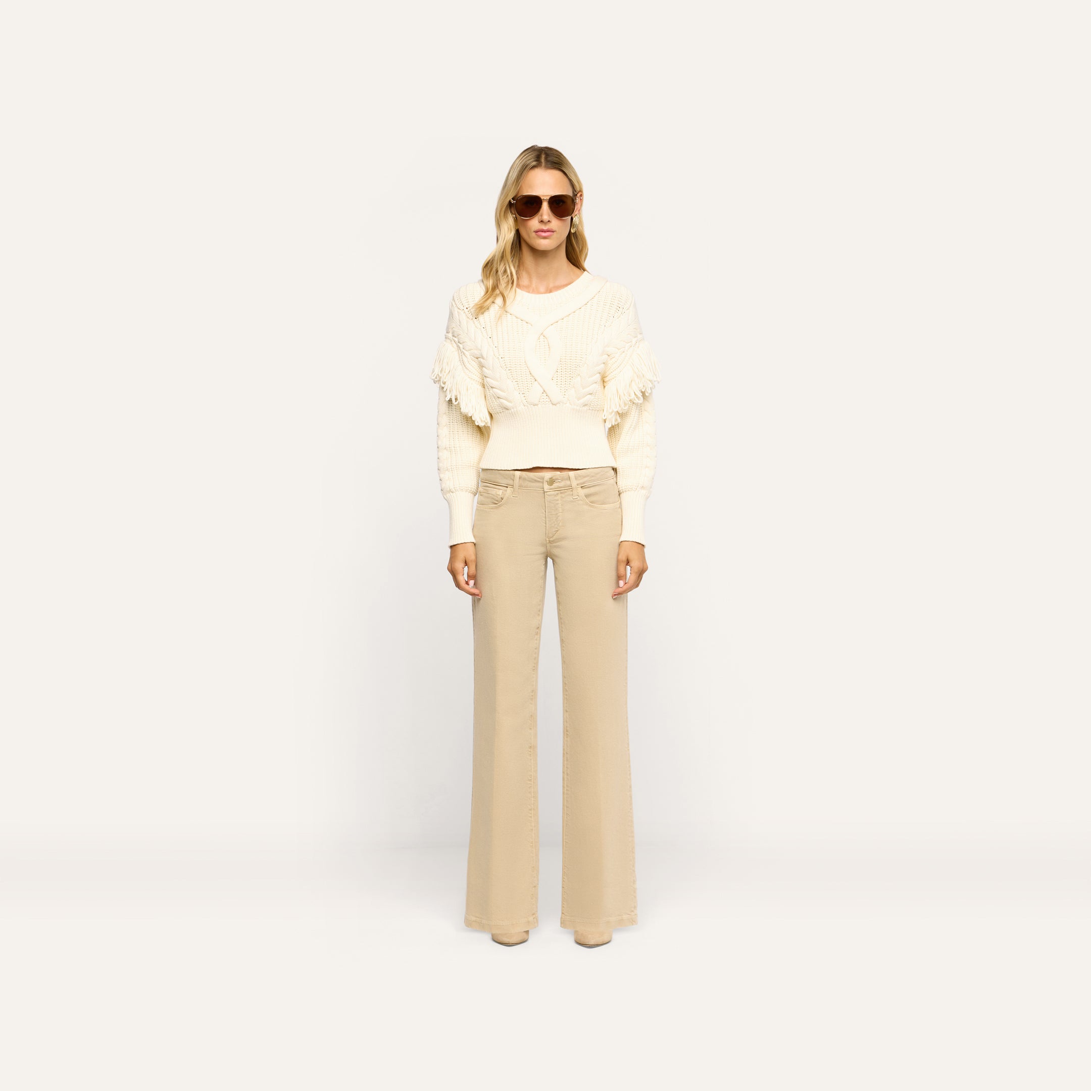A person wearing a white cable-knit fringe sweater and tan Joanne Low-Rise Wide-Leg Jean.