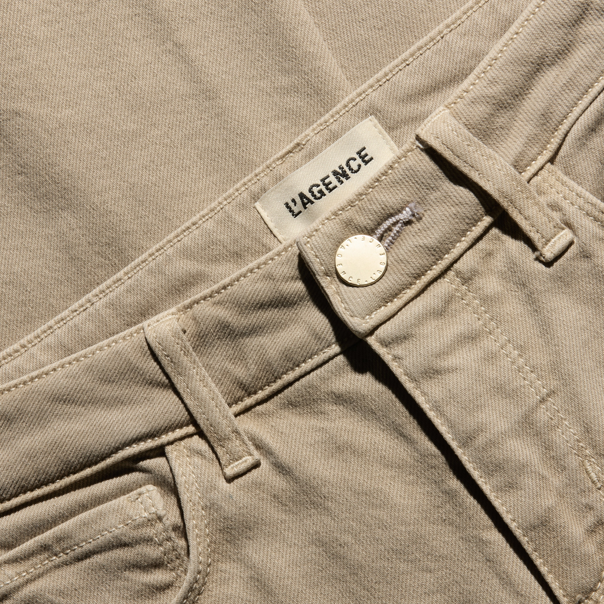 Close-up of the waistband of the tan, low-rise Joanne Low-Rise Wide-Leg Jean in stretch denim, featuring a gold button and a brand label.