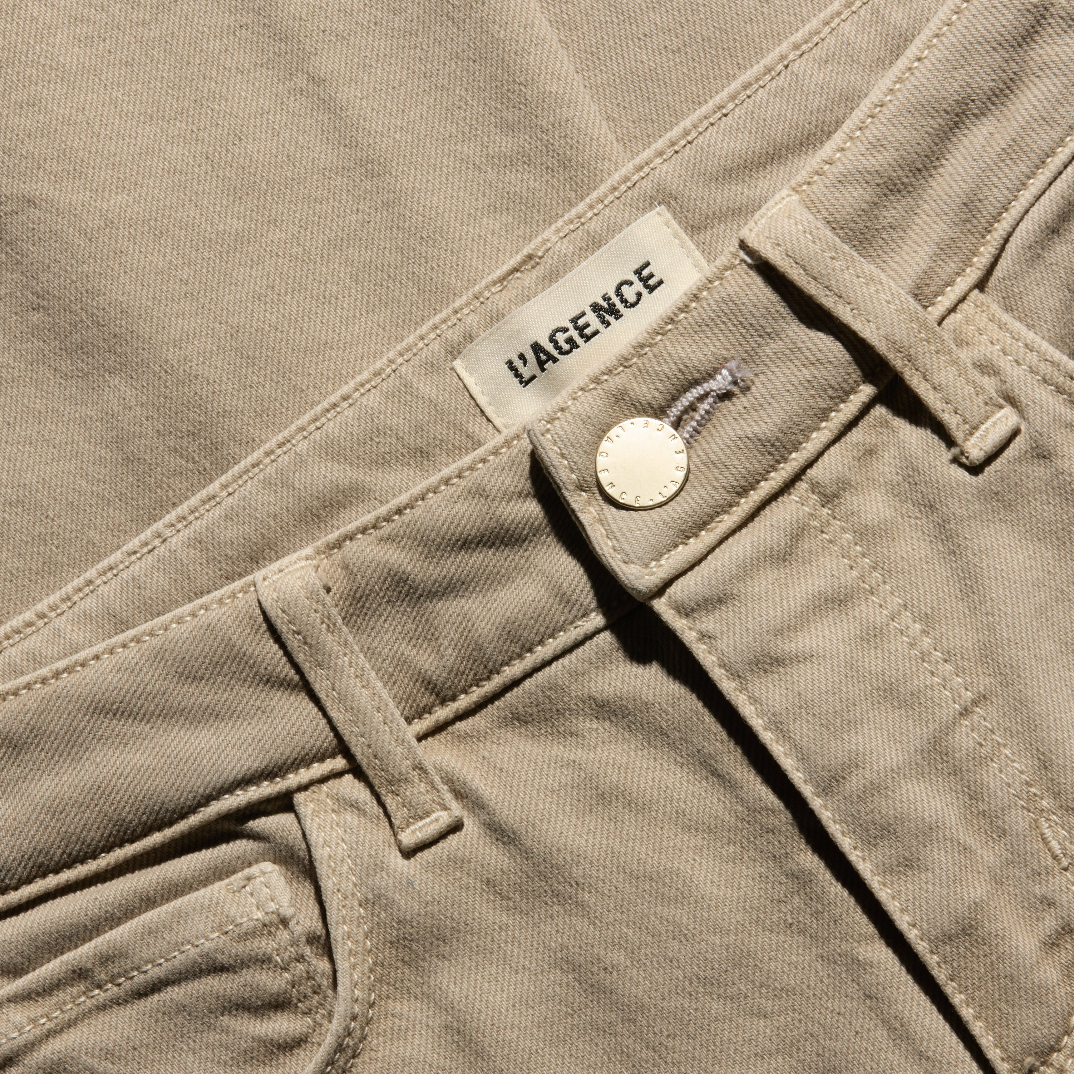 Close-up of the waistband of the tan, low-rise Joanne Low-Rise Wide-Leg Jean in stretch denim, featuring a gold button and a brand label.