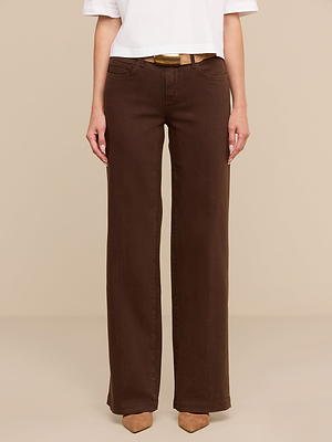 Una persona lleva una camiseta blanca de manga corta, unos vaqueros «Joanne Low-Rise Wide-Leg» de denim elástico marrón y unos zapatos de punta de color beige, de pie frente a un fondo beige. La foto está recortada a la altura de los hombros.