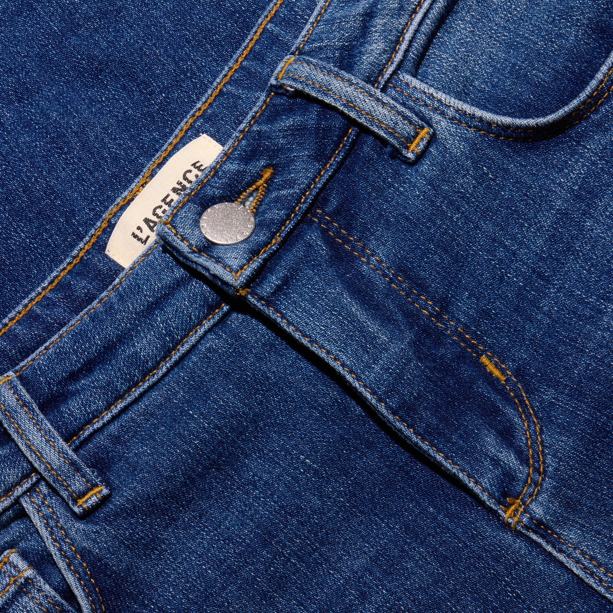 Close-up of the waistband and fly of indigo wash, low-rise Joanne Low-Rise Wide-Leg Jean, featuring a brand label near the top button.