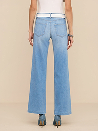 Une personne est représentée de dos sur un fond beige uni. Elle porte un jean Joanne Low-Rise Wide-Leg de couleur indigo clair, un haut blanc, des talons bleus et des bracelets.