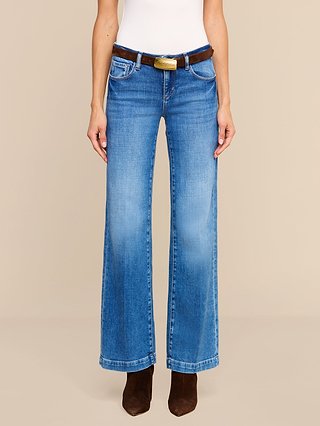 Person wearing Joanne Low-Rise Wide-Leg Jean crafted from stretch denim with a brown belt and dark brown boots, standing against a plain beige background. The photo is cropped at the shoulders.