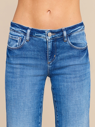 Close-up of a person wearing the Joanne Low-Rise Wide-Leg Jean in blue stretch denim, highlighting the waistband, button, and front pockets. The person’s midriff is visible, while their face and upper body are not shown.