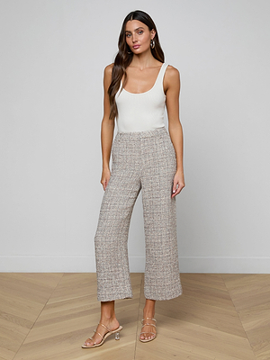 A woman with long hair and minimal accessories stands against a plain wall in a sleeveless white top, strappy heeled sandals, and the high-waisted Lula Cropped Tweed Trouser.