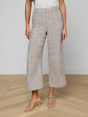 A person wears Lula Cropped Tweed Trousers and strappy heeled sandals, standing on a light wood floor against a plain white wall, with only the lower half of their body visible.
