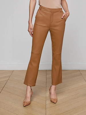 A woman stands on a wooden floor wearing the tan Ketra Leather Bootcut Trouser and matching heels, with one hand in her pocket. Her upper body is mostly out of frame.