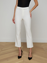 A woman is wearing the Ketra Bootcut Trouser in high-waisted white stretch suit fabric, styled with black heels and a black sleeveless top, standing against a plain light background. Only her body from the shoulders down is visible.