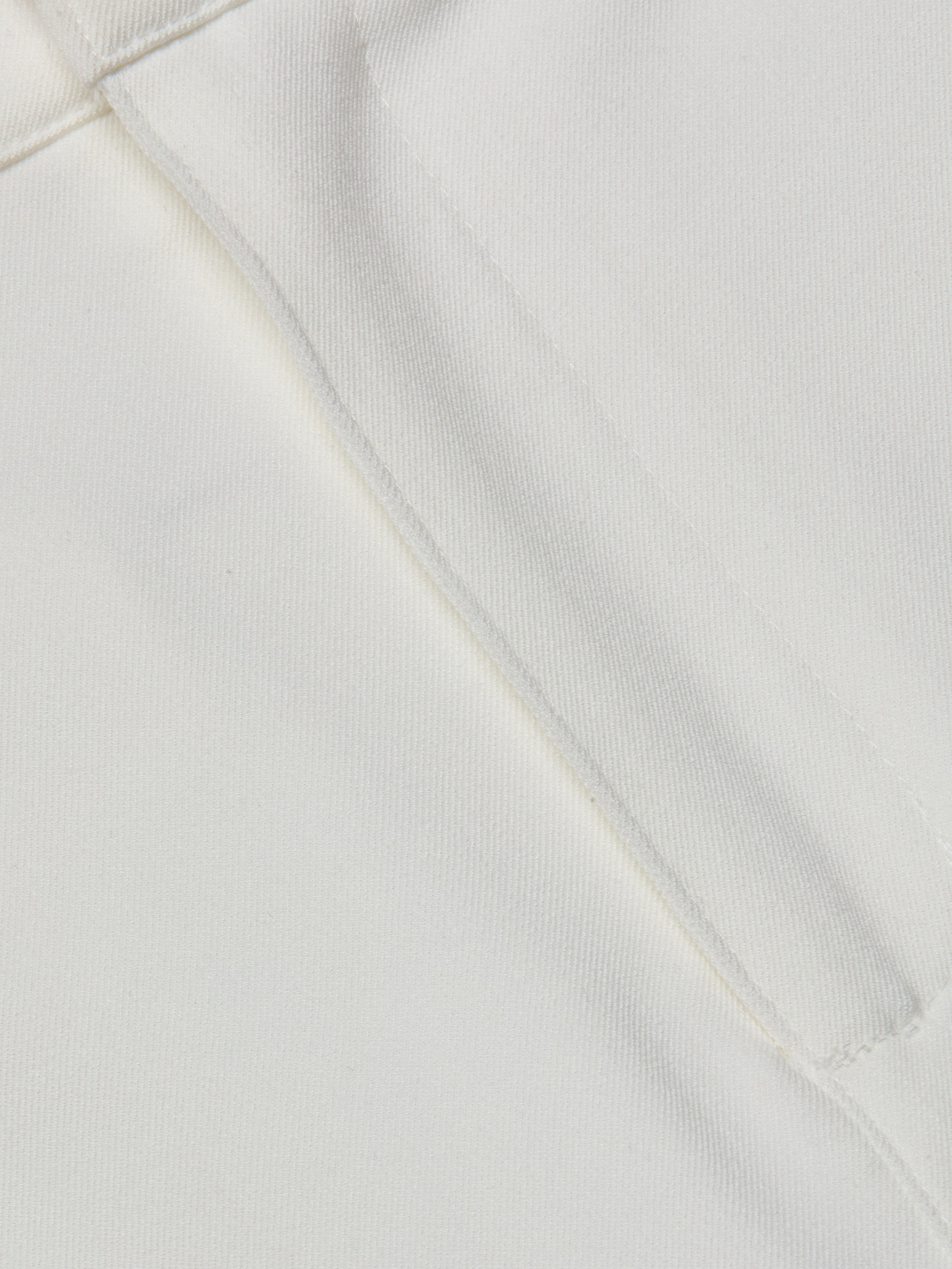 Close-up of the white stretch fabric from the Ketra Bootcut Trouser, featuring a visible seam and stitching. The texture and weave of the material are clearly shown.