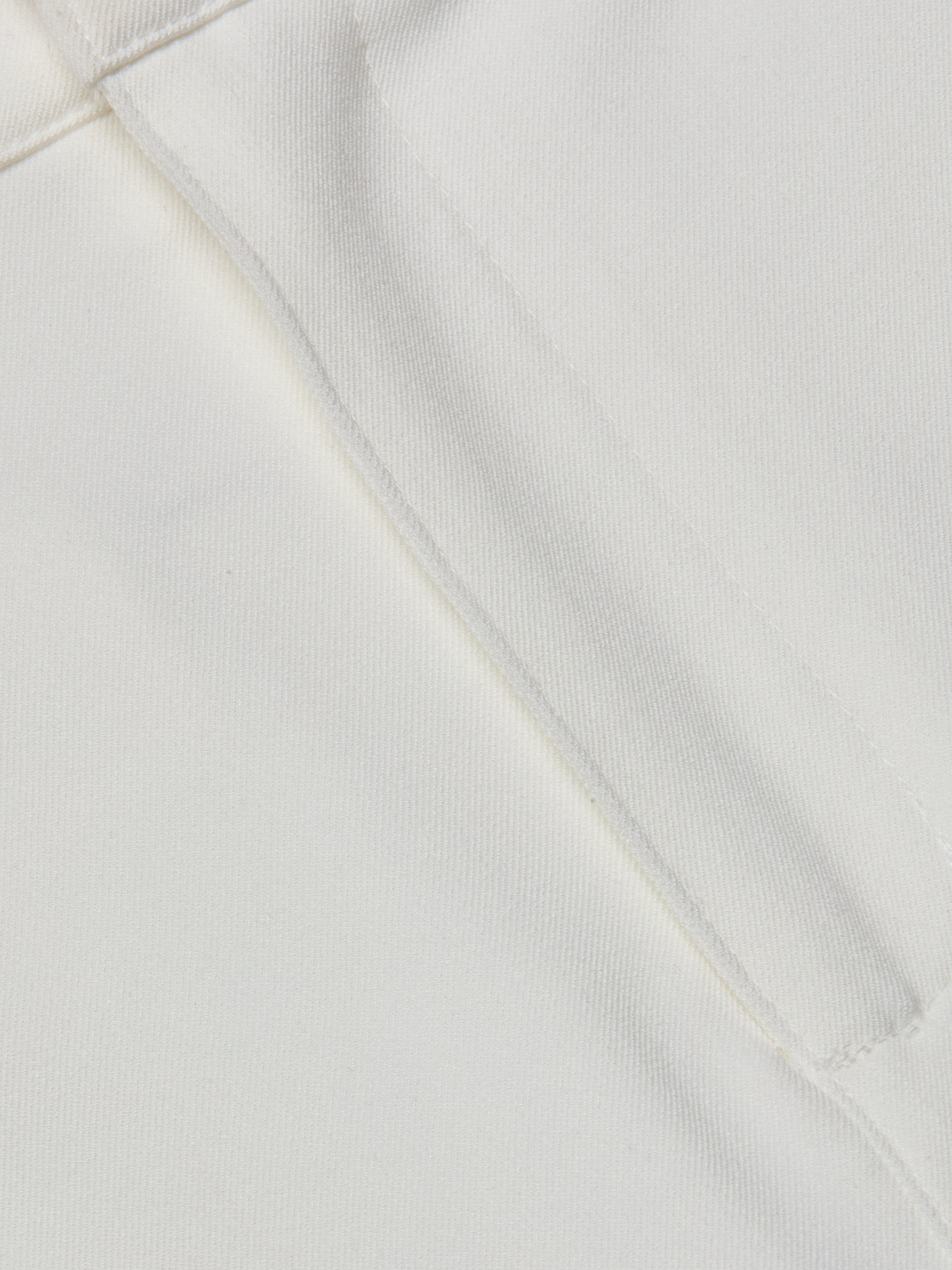 Close-up of the white stretch fabric from the Ketra Bootcut Trouser, featuring a visible seam and stitching. The texture and weave of the material are clearly shown.