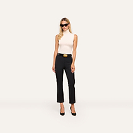 A woman with long blonde hair, sunglasses, a sleeveless white turtleneck, and the Ketra Bootcut Trouser with a wide belt and slant pockets stands against a plain light background.
