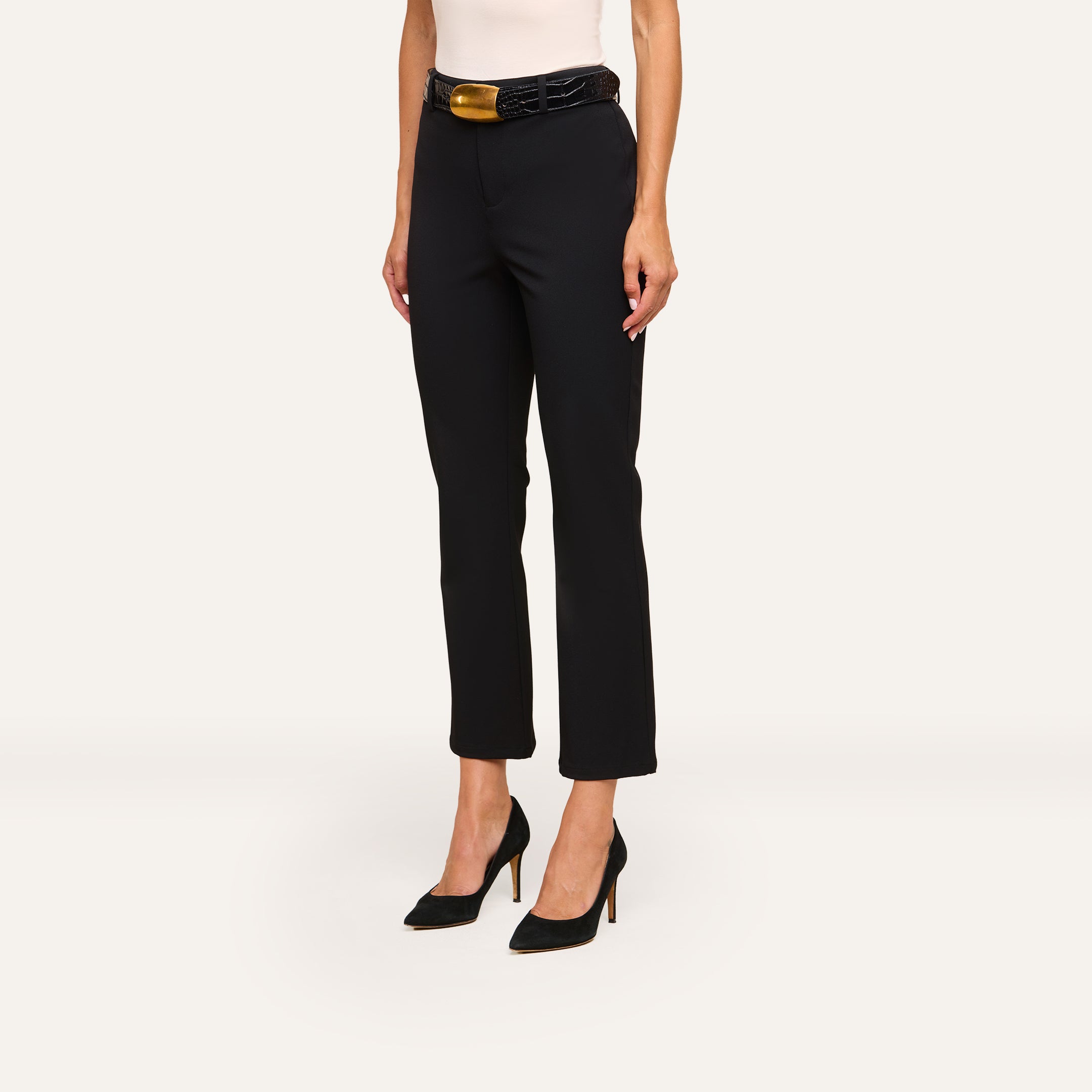 A woman wears Ketra Bootcut Trouser in black with slant pockets, paired with a wide black belt and black high heels. Only her lower torso and legs are visible against a plain off-white background.