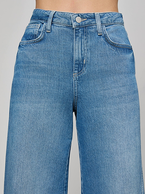 Close-up of a person wearing L'AGENCE Beau Wide-Leg Jean, featuring high-rise blue stretch denim with waistband, front button, zipper, belt loops, and front pockets against a plain background.