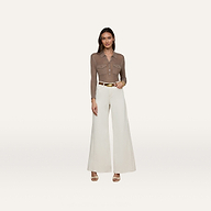 A woman stands against a plain white background wearing a brown collared long-sleeve shirt, the Beau Wide-Leg Jean in high-rise stretch cotton twill in white, a white belt with a gold buckle, and beige heels.