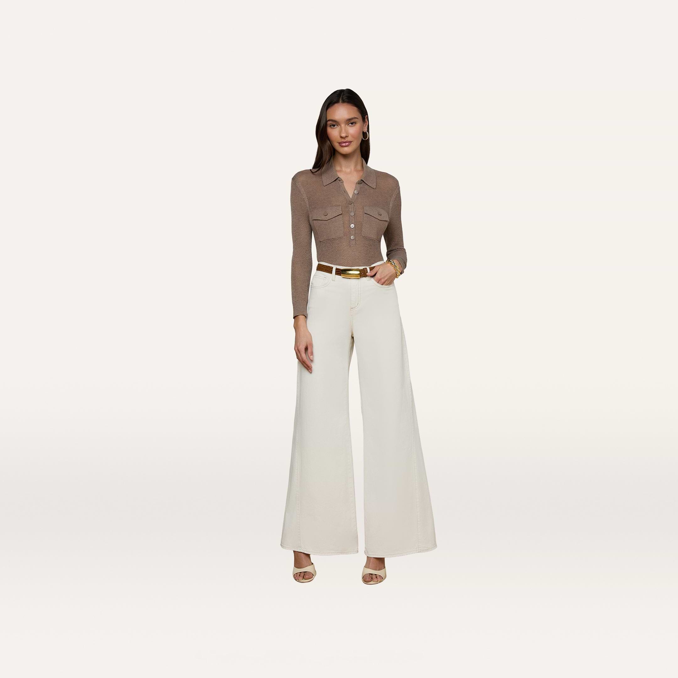 A woman stands against a plain white background wearing a brown collared long-sleeve shirt, the Beau Wide-Leg Jean in high-rise stretch cotton twill in white, a white belt with a gold buckle, and beige heels.