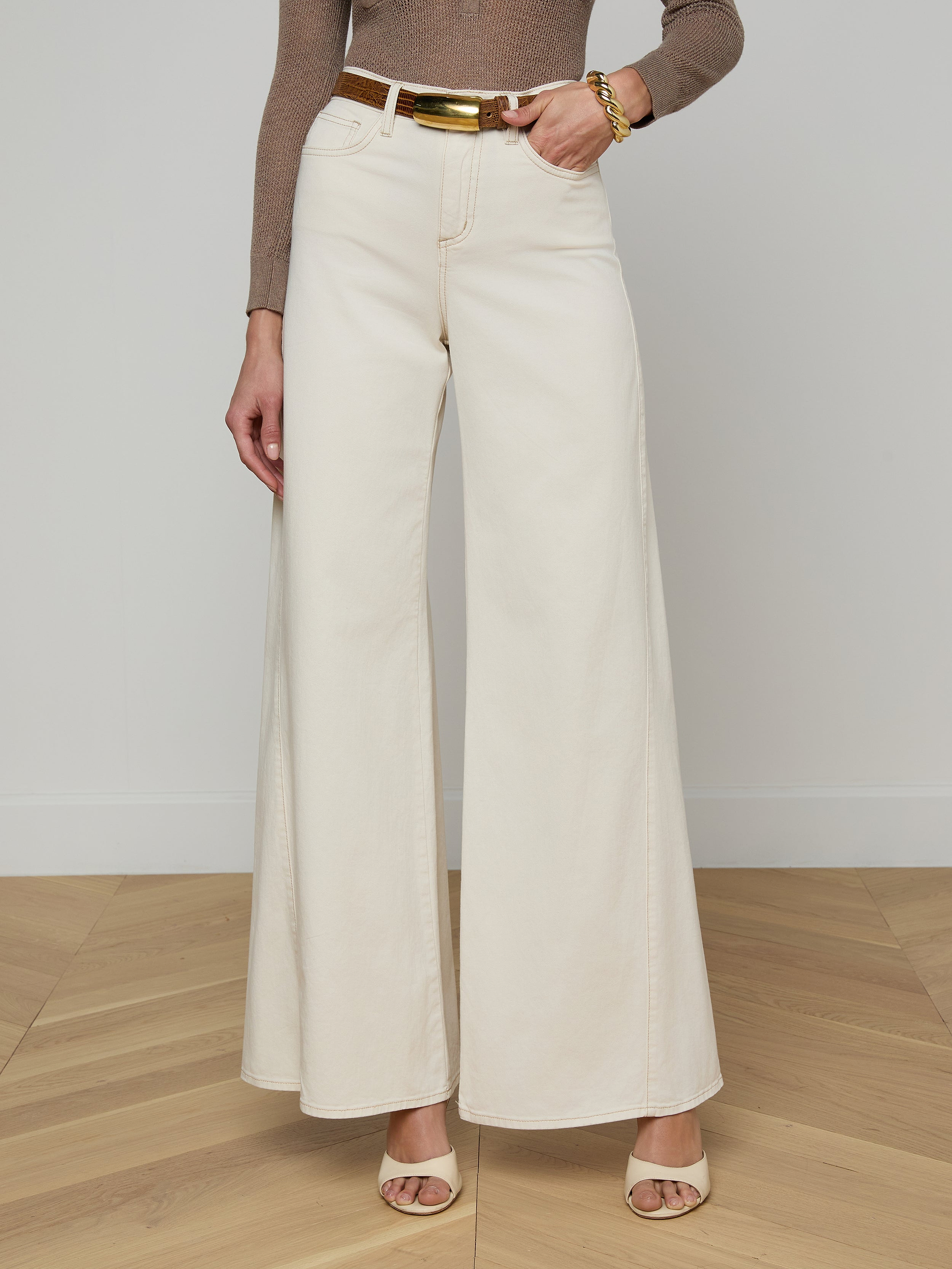 A person wearing the Beau Wide-Leg Jean in cream stretch cotton twill, paired with a brown long-sleeve top, beige heeled sandals, and a gold bracelet, standing against a plain white background.