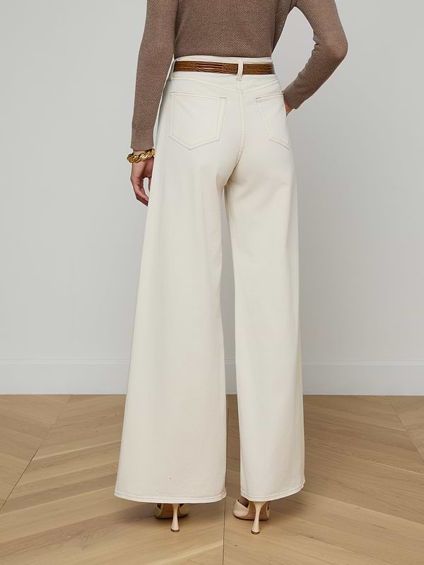 A person wearing the Beau Wide-Leg Jean in high-rise, wide-leg white stretch cotton twill, paired with a brown long-sleeve top and heeled shoes, shown from the back against a plain white background.