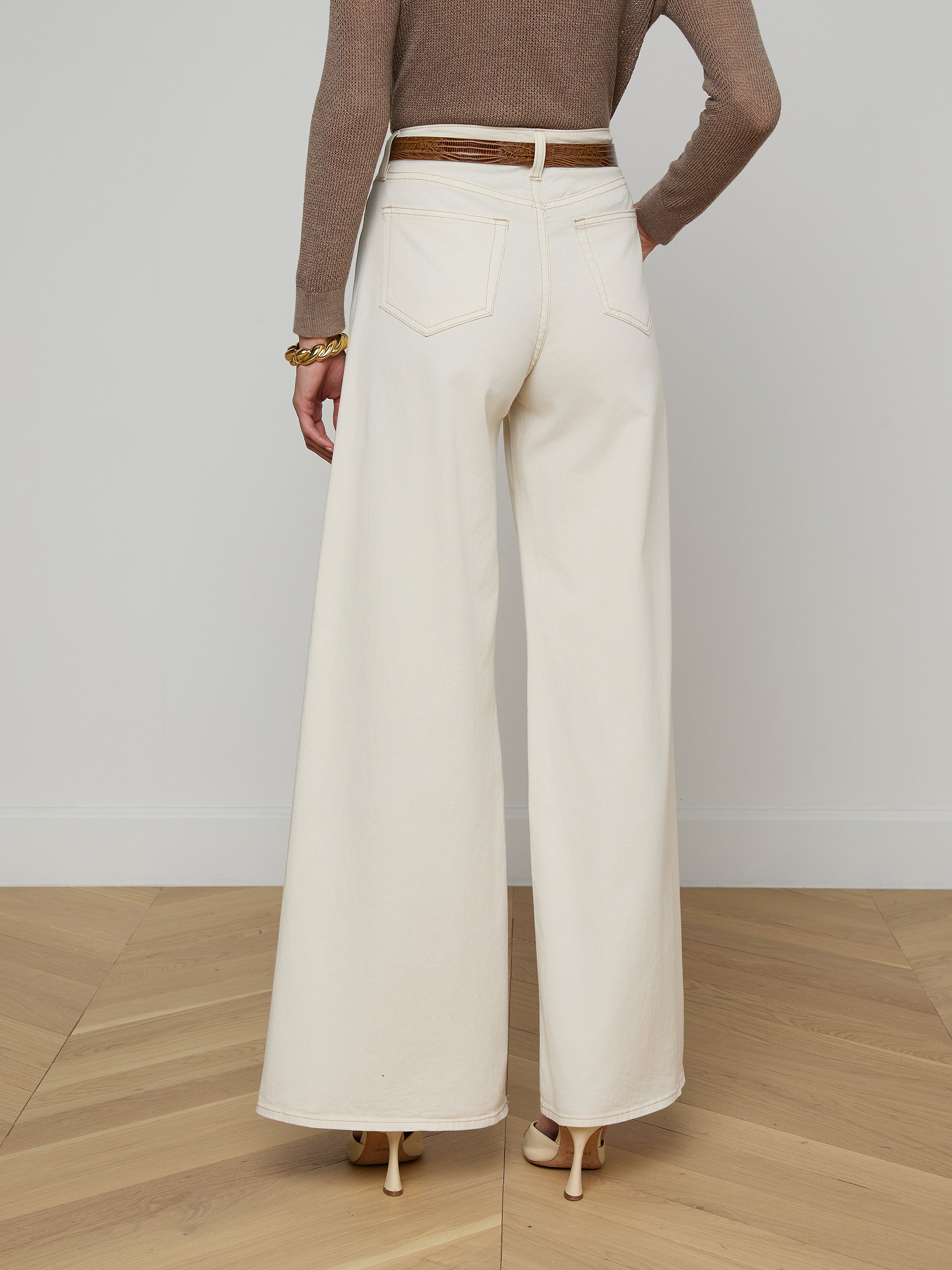 A person wearing the Beau Wide-Leg Jean in high-rise, wide-leg white stretch cotton twill, paired with a brown long-sleeve top and heeled shoes, shown from the back against a plain white background.