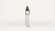 Woman wearing a white sleeveless top and wide-leg white pants, standing with hands in pockets against a plain white background.