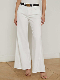 A person is shown from the waist down, wearing the Beau Wide-Leg Jean in white paired with a black belt and open-toed heels, standing against a plain light background. The upper body and face are not visible.
