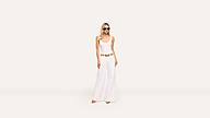 A woman wearing sunglasses, a white sleeveless top, and wide-leg white pants with a tan belt stands stylishly against a plain white background.