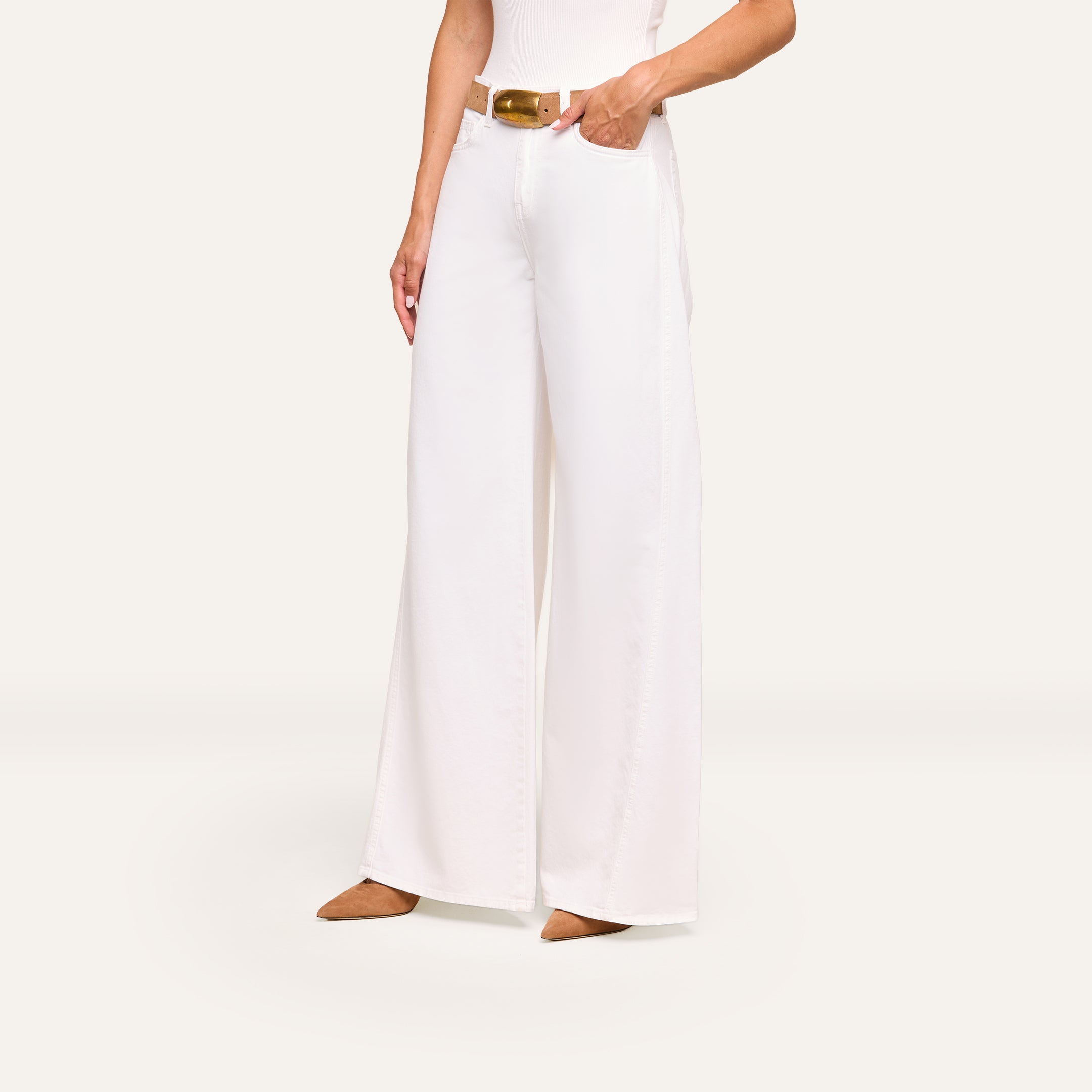 Wearing the Beau Wide-Leg Jean with a brown belt and pointed shoes, this person poses with one hand in their pocket against a plain background.