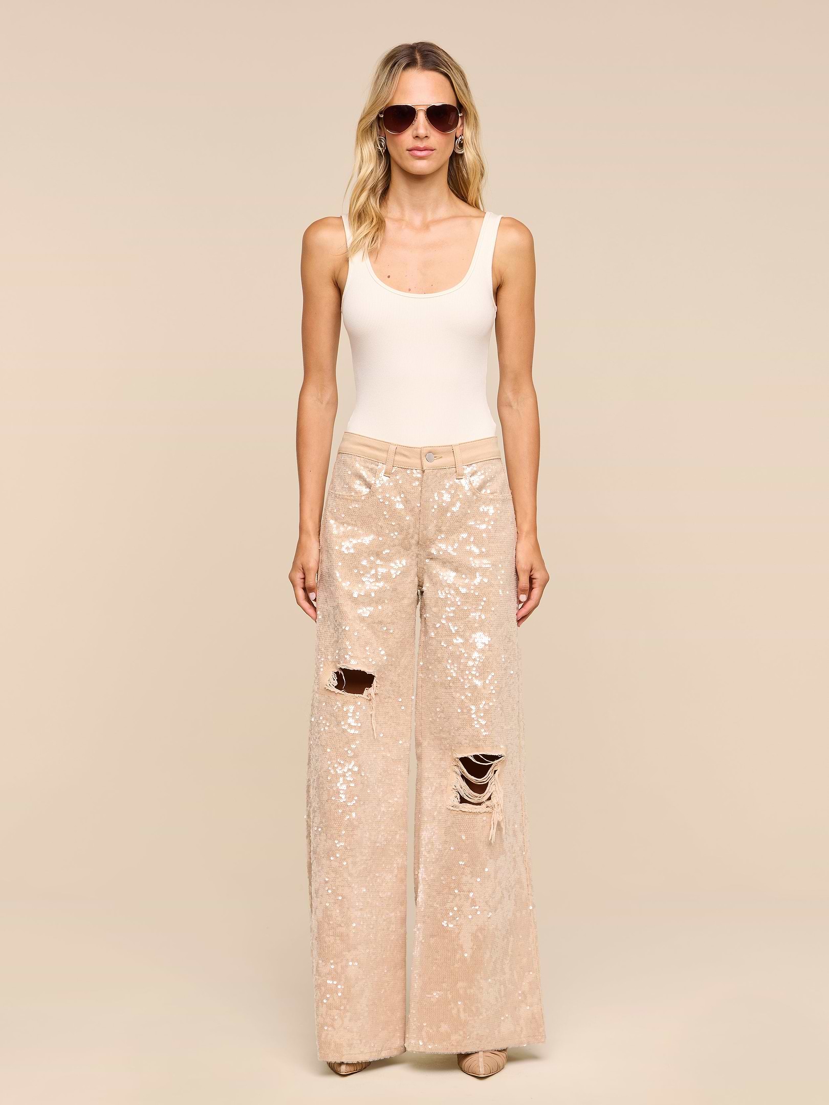 A woman in sunglasses, a white tank top, and the Quincy Embellished Wide-Leg Jean with distressed knees stands against a plain white background.