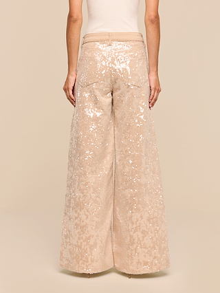 A person wearing the Quincy Embellished Wide-Leg Jean, featuring a high-rise, wide-leg silhouette with beige sequins, paired with a sleeveless beige top and shown from the back against a plain beige background.