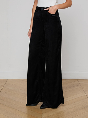 A person wearing the Quincy Wide-Leg Corduroy Pant in black and black pointed-toe shoes stands on a wooden floor against a plain white wall, with only their lower torso and legs visible.