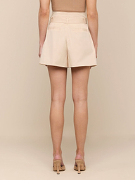 A person stands facing away, wearing a tan sleeveless top, the Damira Poplin Short featuring an ultra-high waist and self-tie belt, and tan high-heeled sandals against a plain light background.