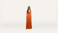 A woman wearing sunglasses and an orange sleeveless jumpsuit stands against a plain white background.