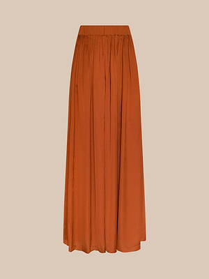 The Haylo Pant, a long, flowy rust-orange style with an elastic waistband reminiscent of high-waist pants, is displayed against a beige background.