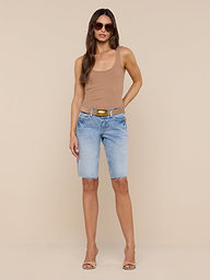 A woman stands against a plain white background wearing sunglasses, a tan sleeveless top, heeled sandals, and the Elise Jean Bermuda Short—light blue low-rise shorts crafted from all-cotton denim with a relaxed fit.