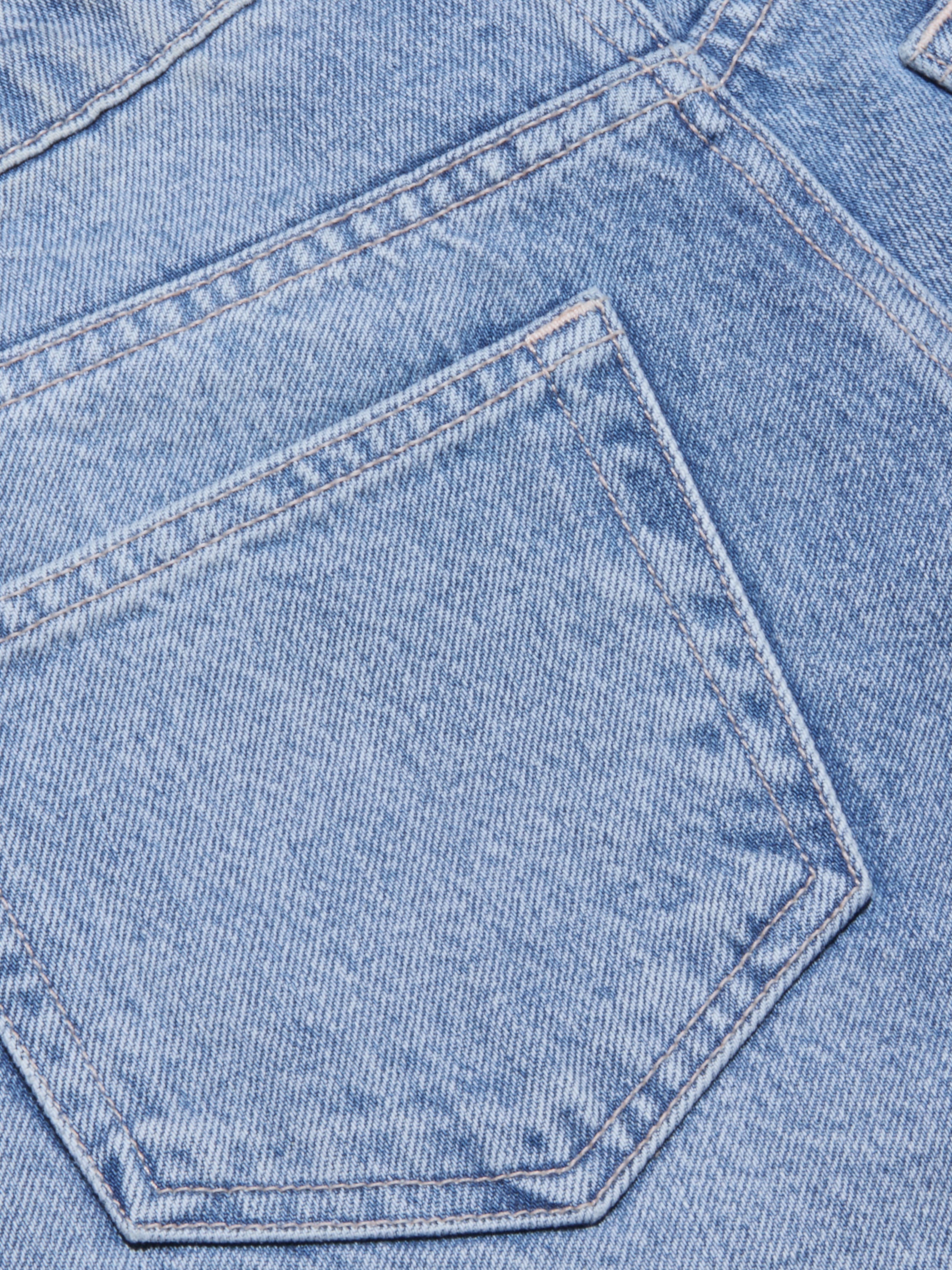 Close-up of light blue all-cotton denim fabric showing a pocket and visible stitching details on the Elise Jean Bermuda Short.