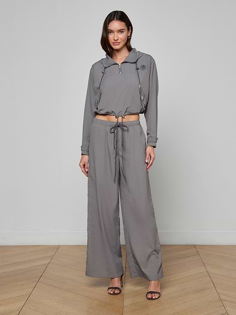 A woman stands against a plain white background, wearing a gray, long-sleeve cropped jacket and matching Valkyrie Snap Pant with black open-toe heels.