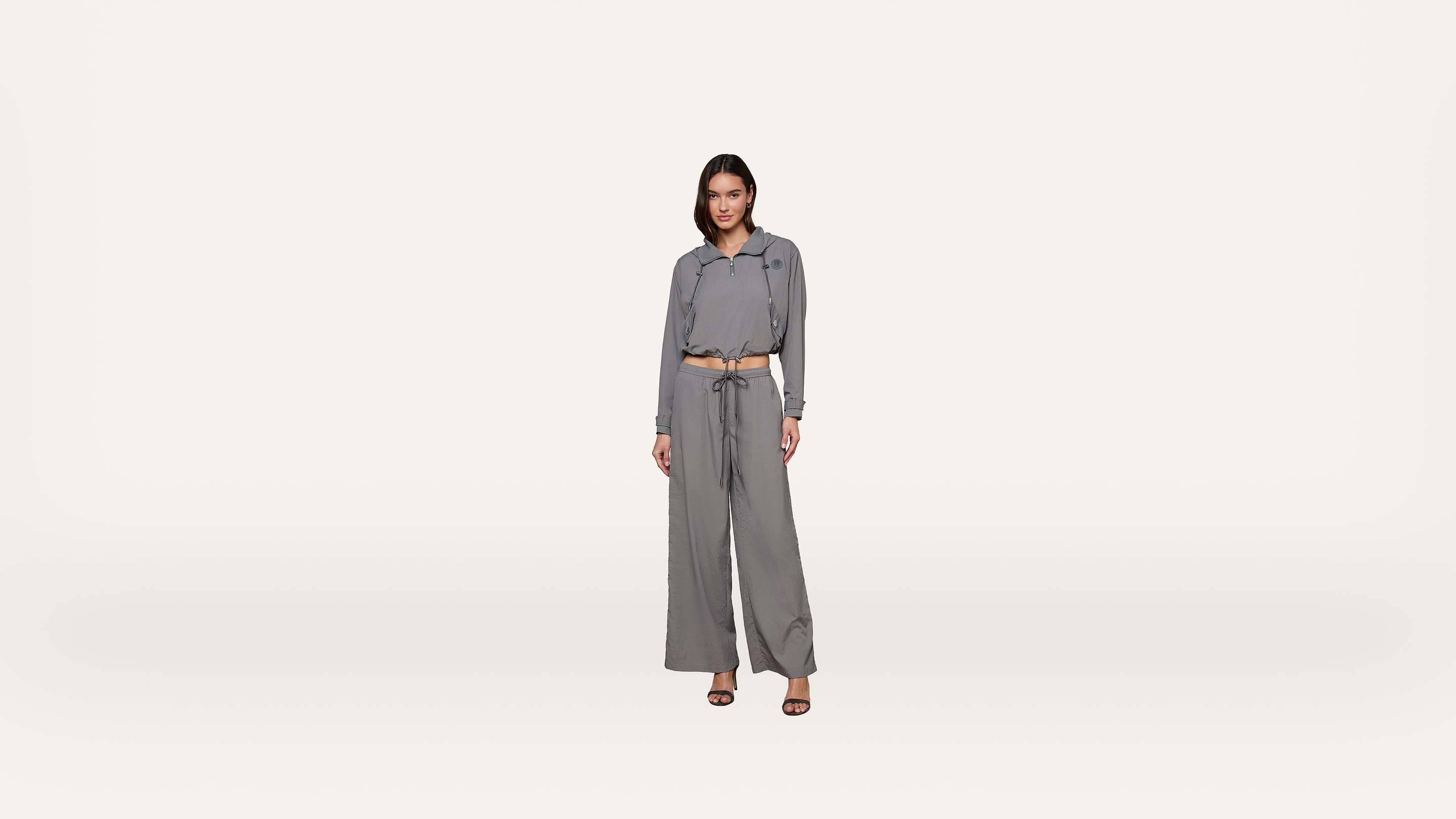 A woman stands facing forward, wearing a matching gray long-sleeve button-up shirt and wide-leg pants with a tie belt, and black heels, against a plain white background.