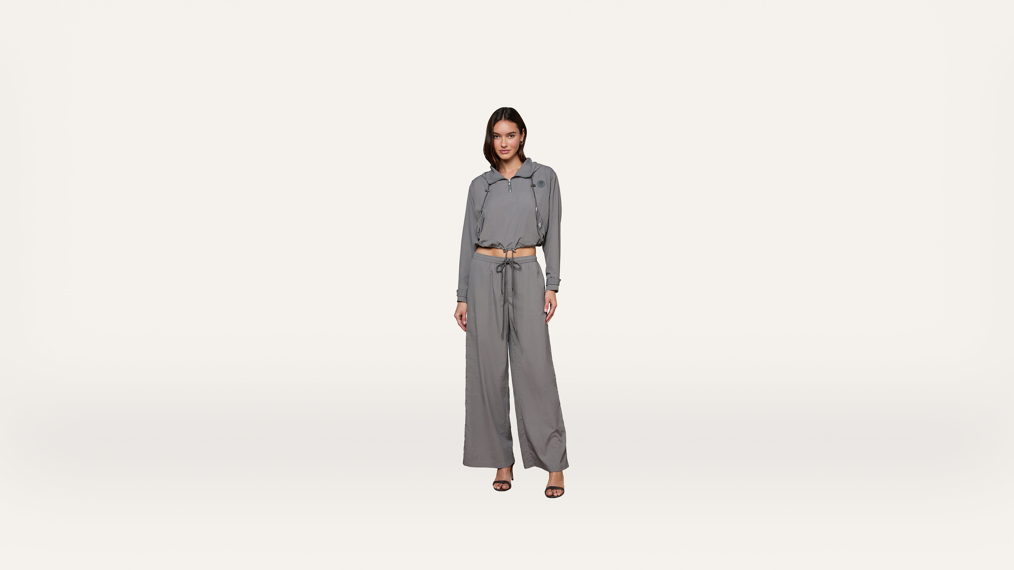 A woman stands facing forward, wearing a matching gray long-sleeve button-up shirt and wide-leg pants with a tie belt, and black heels, against a plain white background.