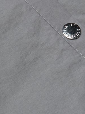 Close-up of the Valkyrie Snap Pant’s light gray textured fabric, featuring a silver metallic button with embossed text, sewn near a seam with visible white stitching.