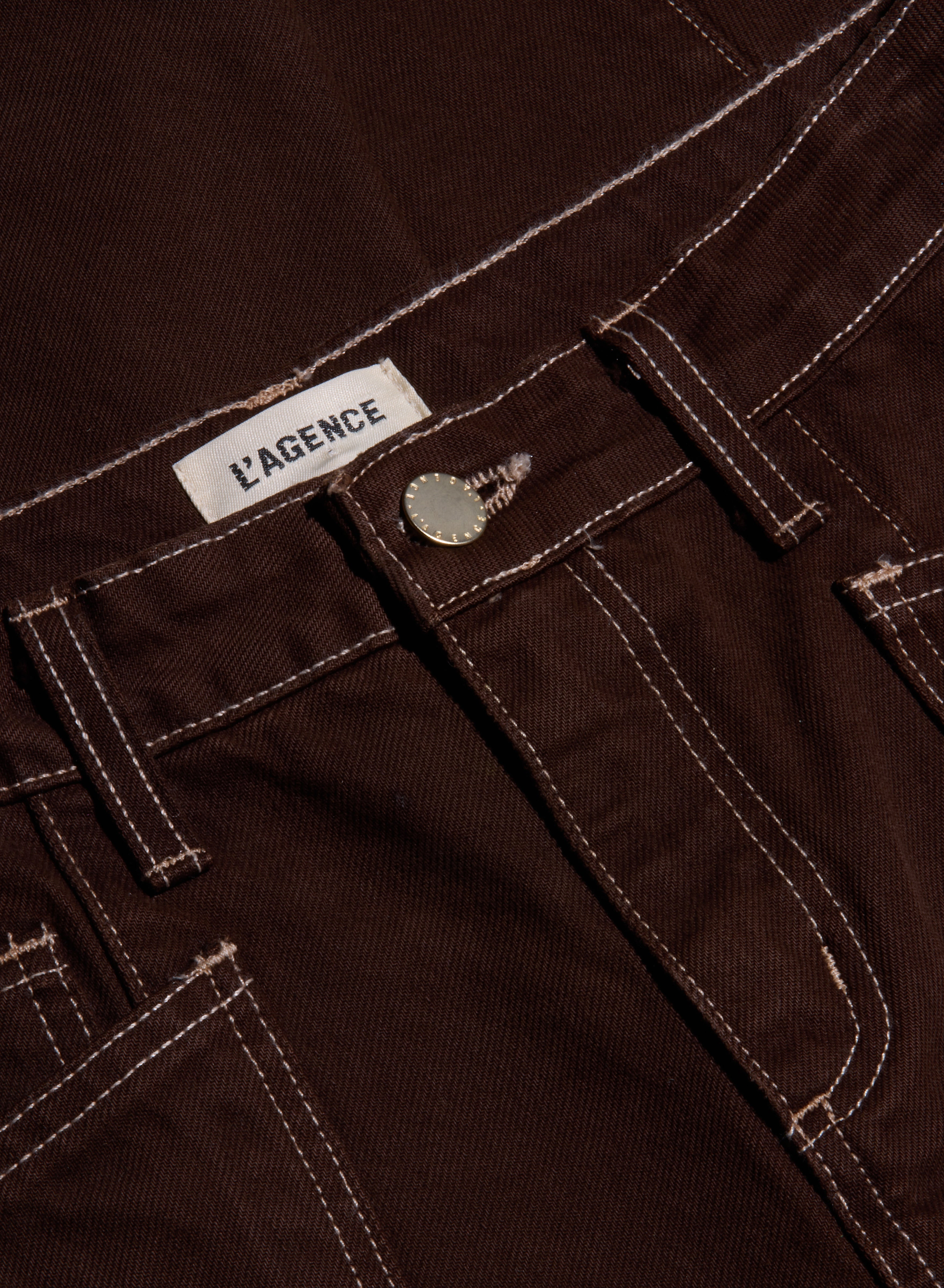 Close-up of the Cody Cropped Barrel-Leg Jean in brown high-rise denim, featuring white stitching, a metal button, and a visible L’AGENCE brand label on the waistband. Crafted from non-stretch denim with a modern barrel-leg silhouette.