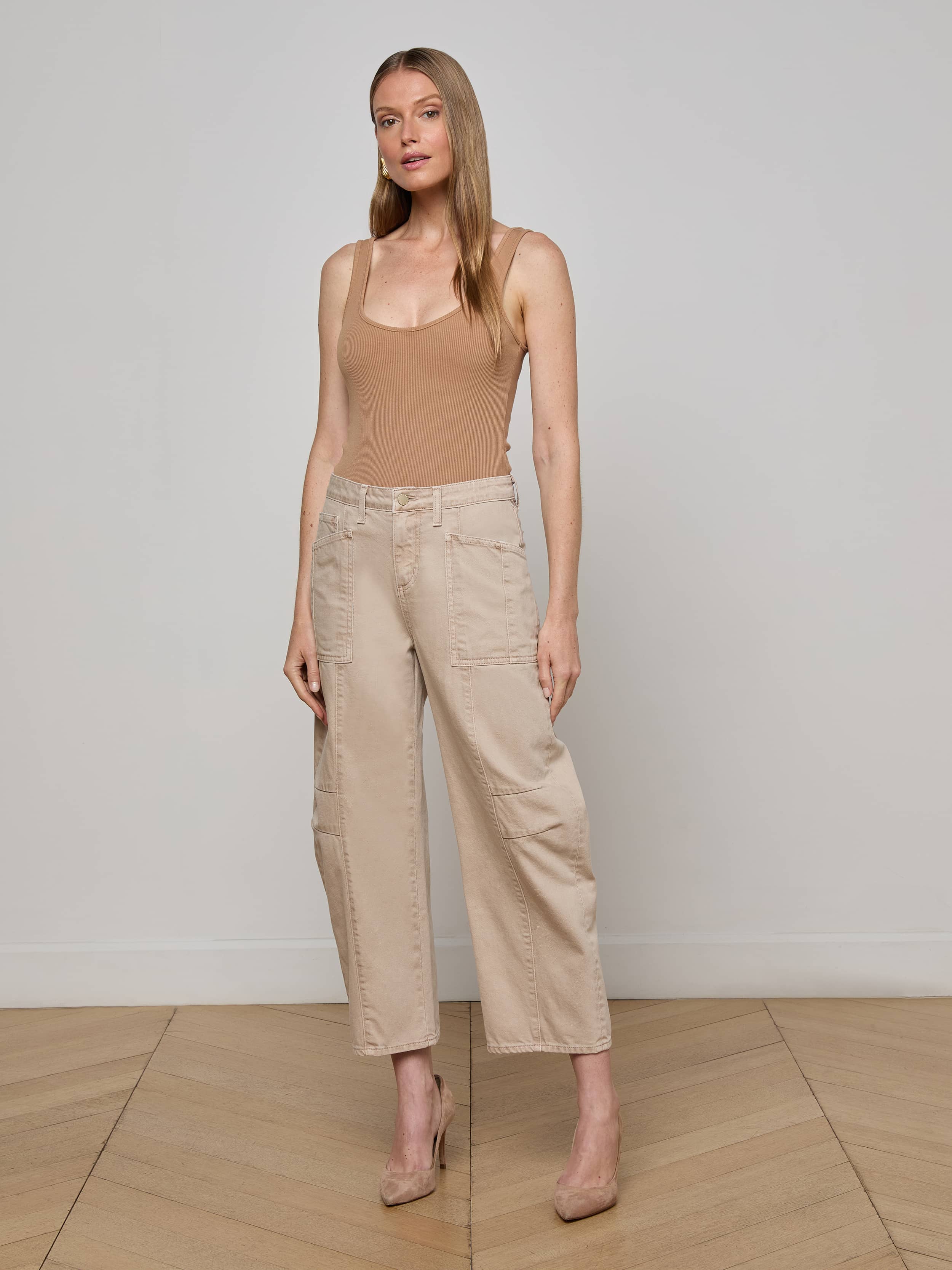 A woman stands against a plain white background wearing a tan sleeveless top, nude heels, and the Cody Cropped Barrel-Leg Jean in beige with wide legs and patch pockets.