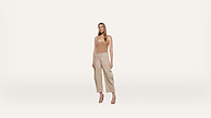 A woman stands against a plain white background, wearing a beige tank top, light-colored wide-leg pants, and beige heels. She faces forward with a neutral expression and her arms relaxed at her sides.