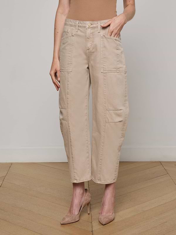 A person models the Cody Cropped Barrel-Leg Jean, featuring patch pockets and a beige hue, paired with nude heels. They stand against a plain white background, with only their lower body visible.